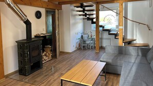 En hyggelig stue med træloft, pejs, sofa og spiseplads med et bord.