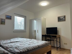 A bedroom with a bed, a desk with a computer, a TV, and a wardrobe.