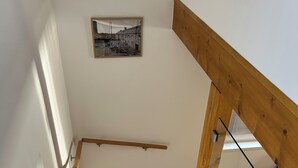 En trætrappe med gelænder, en trægulv med geometrisk mønster, og et billede i ramme på væggen.