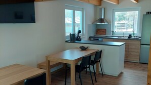 Et moderne køkken med træbjælker, et spiseområde med bord og stole, samt et stort vindue der giver naturligt lys.