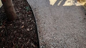 A narrow pathway leading to a white garage door, flanked by wooden fences and a tree. - Private Barwon Heads Cottage | Walk to River (Barwon Heads)