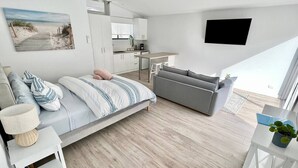 A modern apartment with a bed, a sofa, a dining area, and a kitchen. - Private Barwon Heads Cottage | Walk to River (Barwon Heads)
