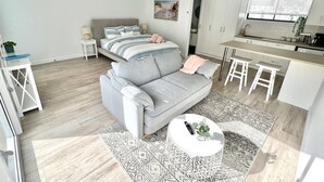 A modern living room with a grey sofa, a round coffee table, and a kitchen area with white cabinets and bar stools. - Private Barwon Heads Cottage | Walk to River (Barwon Heads)
