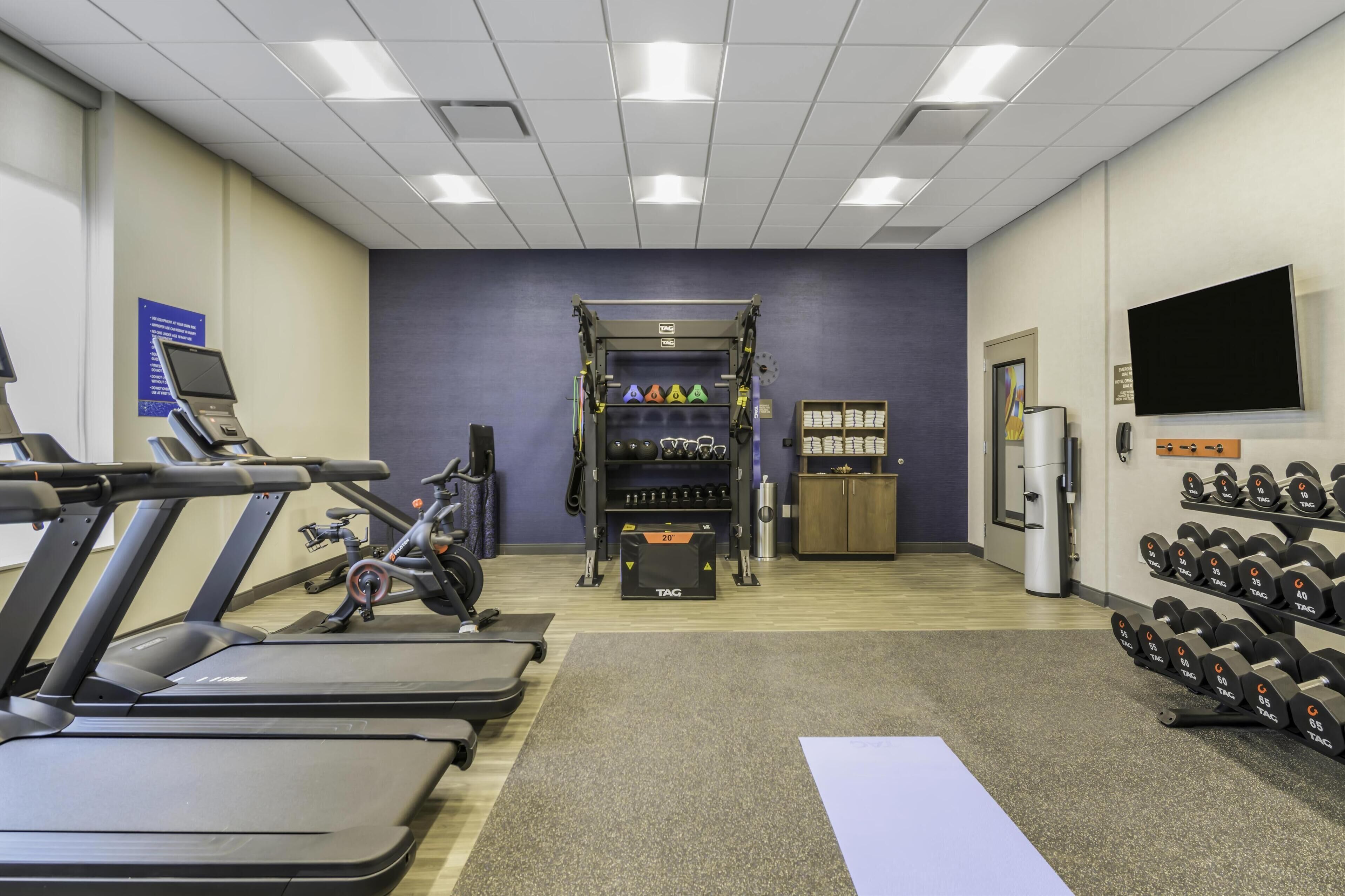 Une salle de sport équipée de tapis de course, d’un banc de musculation, d’un support à squats et d’une variété d’haltères.