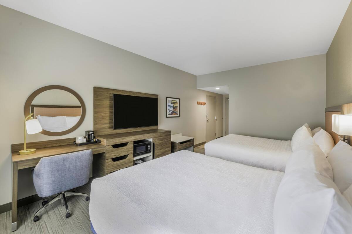 A hotel room with two beds, a desk with a chair, a television, and a microwave.
