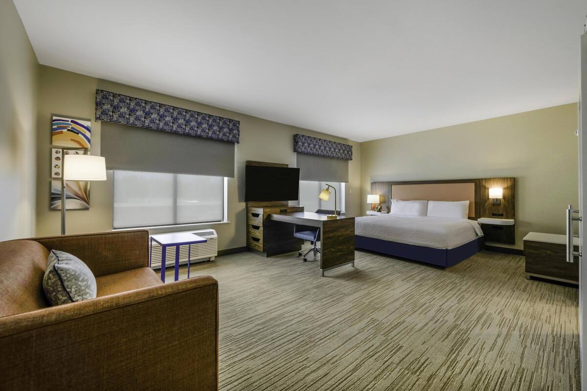 A hotel room with a bed, a desk, a chair, a TV, and a window.