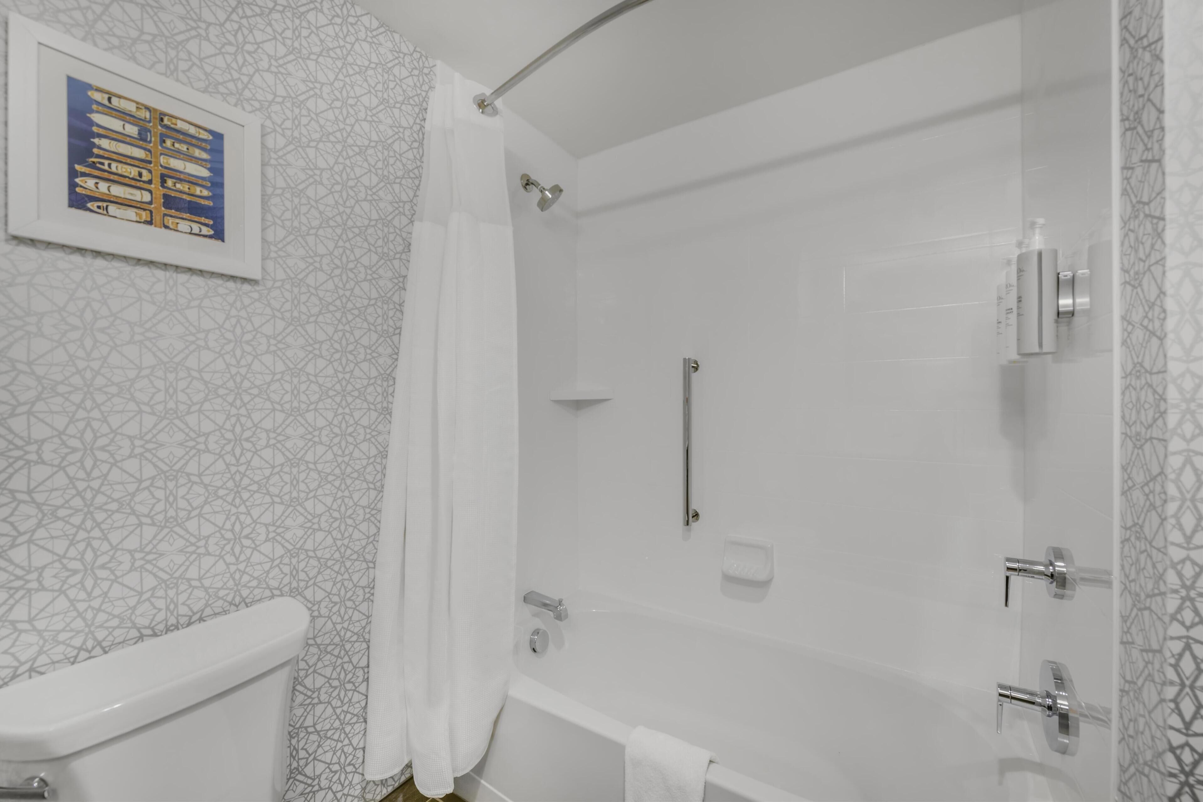 A bathroom with a shower, toilet, and a framed picture on the wall.