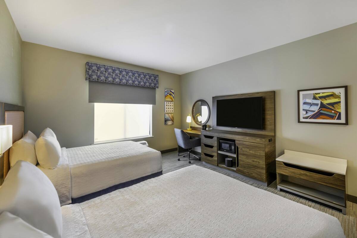 A hotel room with two beds, a desk, a TV, and a large window.