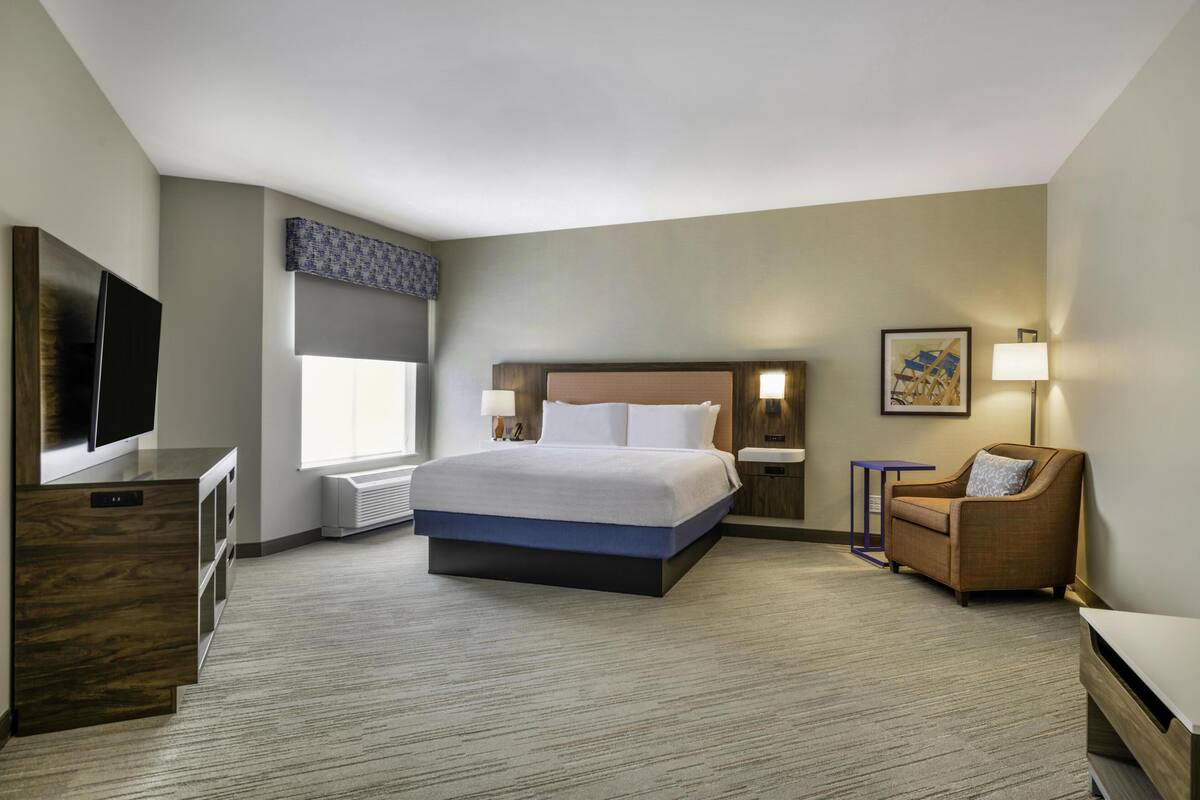A hotel room with a large bed, a TV, a desk, and a chair.