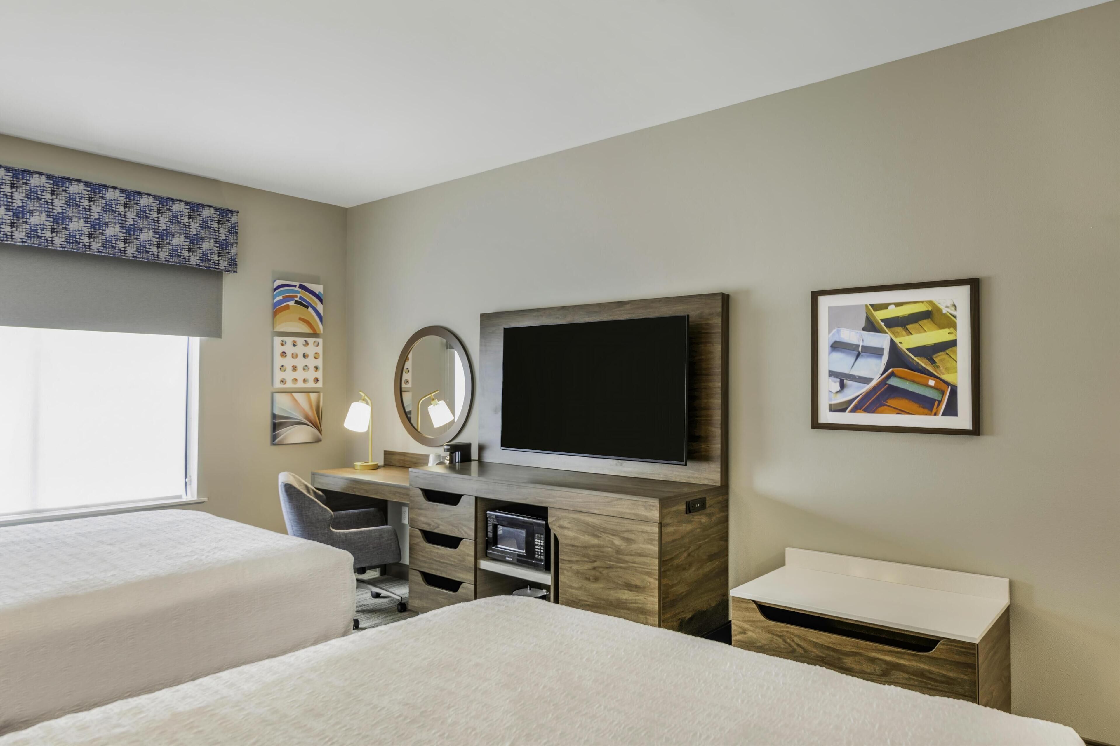 A hotel room with two beds, a desk with a flat-screen TV, a microwave, and a small cabinet.