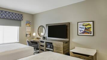 A hotel room with two beds, a desk with a flat-screen TV, a microwave, and a small cabinet.