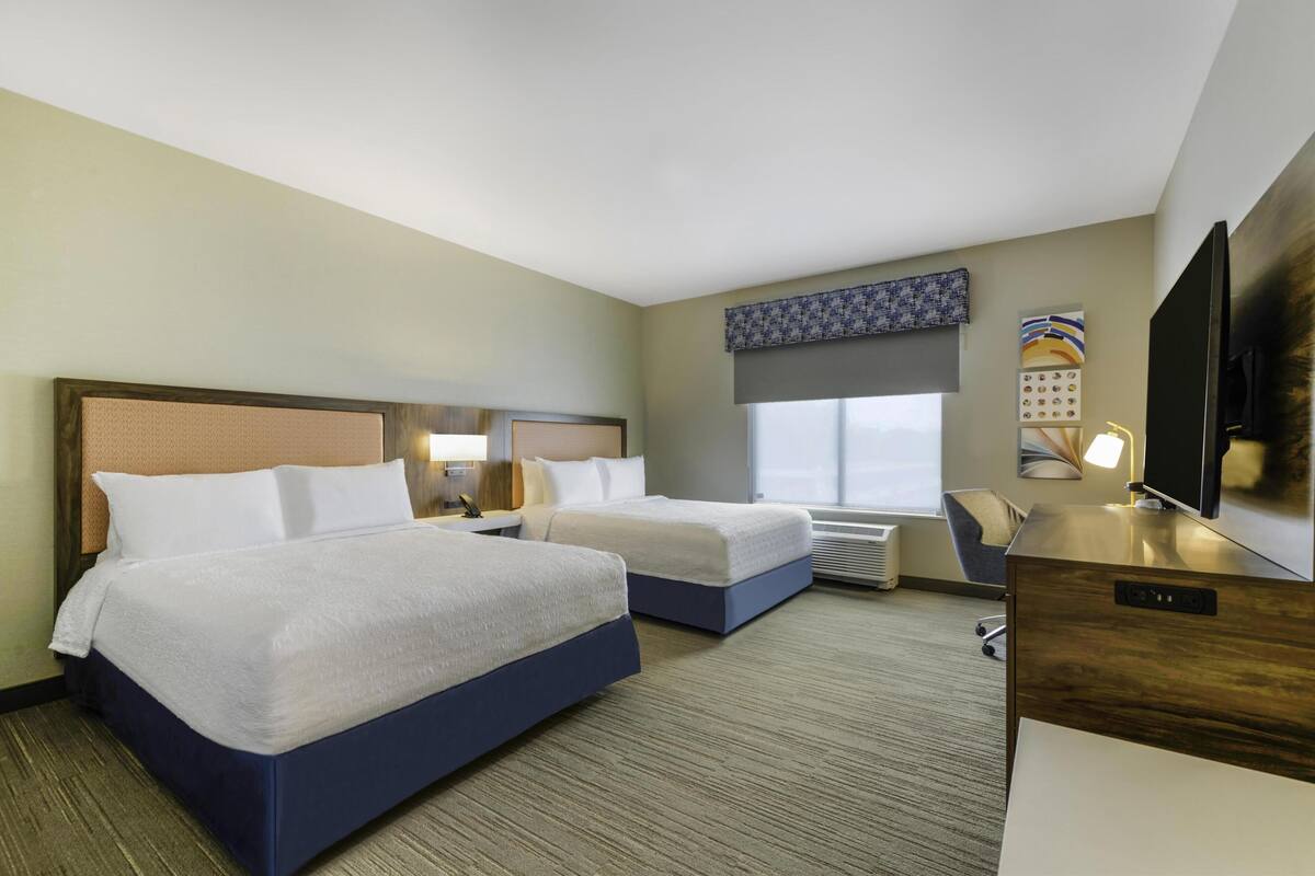 A hotel room with two beds, a desk, a TV, and a window with a view.