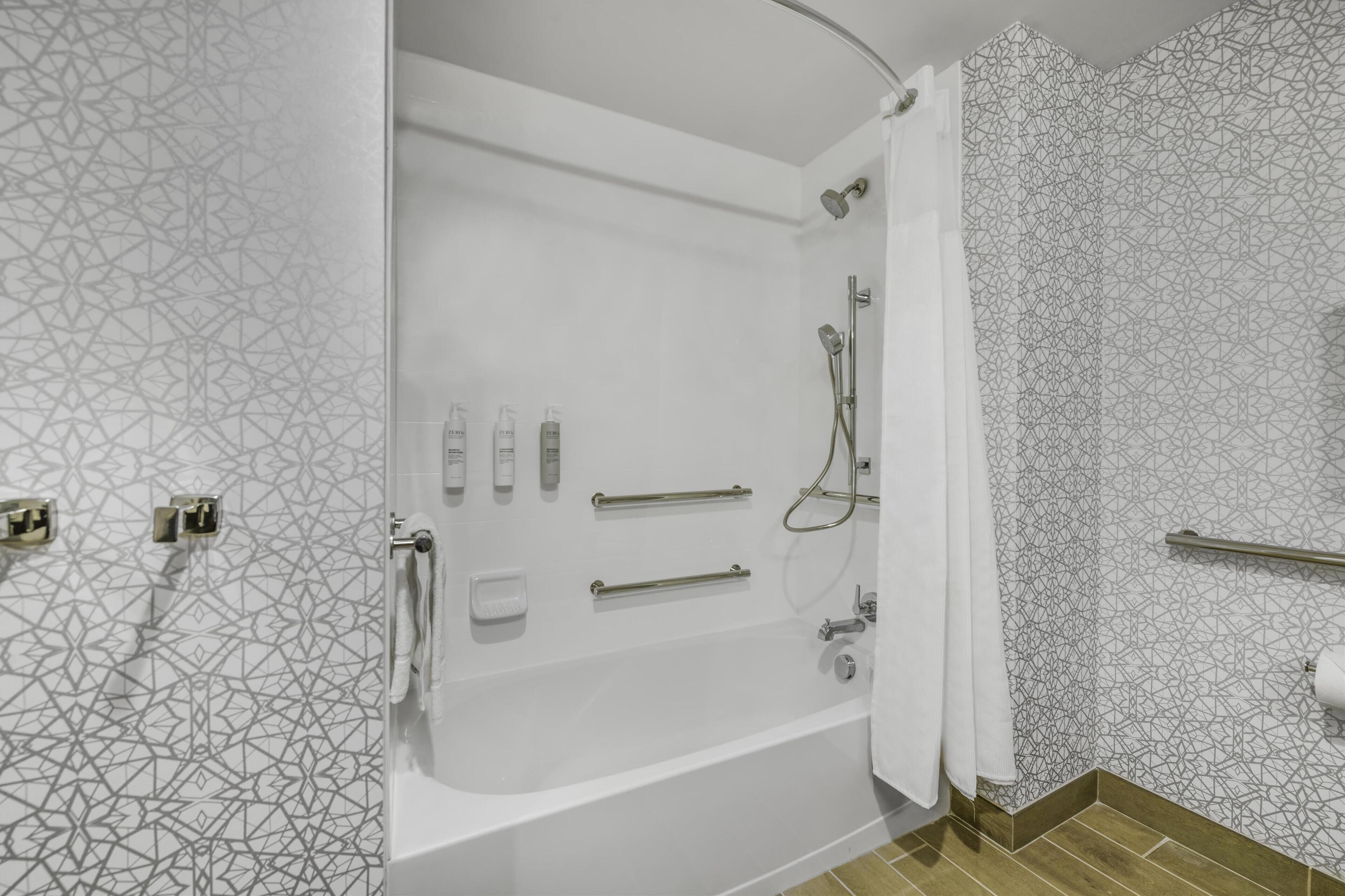 Une salle de bain moderne avec une baignoire sur pieds, des barres d’appui, une pomme de douche et un porte-serviettes.