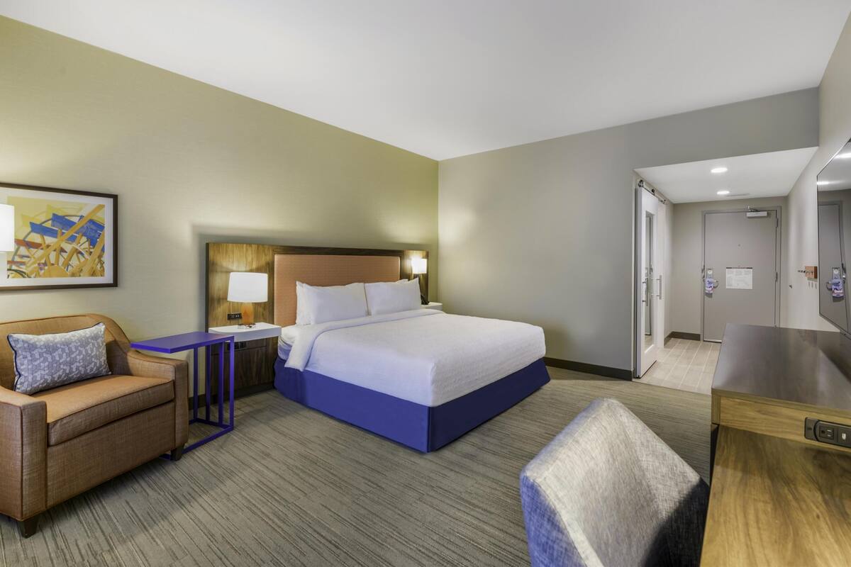 A hotel room with a bed, a desk, a chair, a sofa, and a TV.