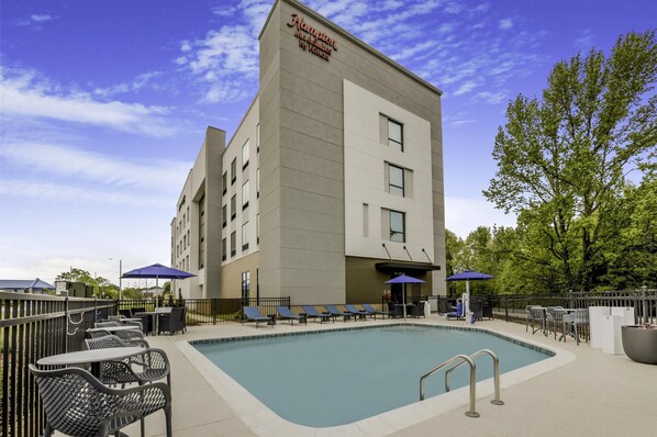 A modern hotel with a swimming pool, outdoor seating, and a clear sky.