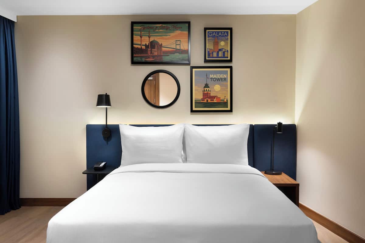 Habitación de hotel con una cama grande, dos mesitas de noche, un espejo redondo y tres cuadros en la pared.