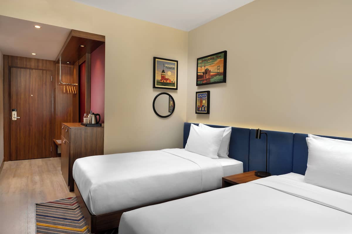Habitación de hotel con dos camas, un armario de madera, una cafetera y decoración en la pared.