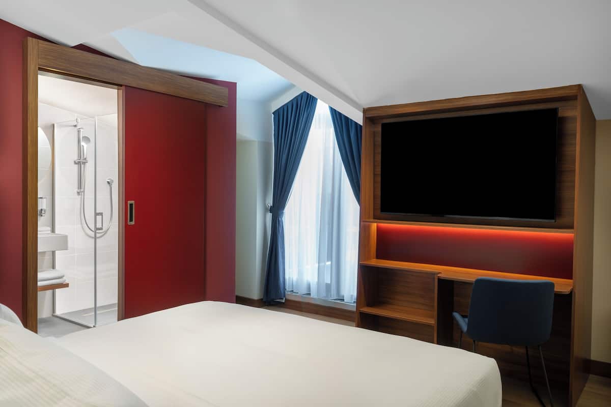 Habitación de hotel con cama, ducha, televisión y escritorio con silla.