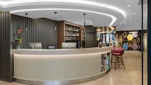 Ein moderner Empfangsbereich mit einer gebogenen Theke, einer Minibar und einer Sitzecke mit roten Stühlen.