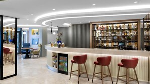 Eine moderne Bar mit einer gebogenen Theke, roten Barhocker und einer Auswahl an Spirituosenflaschen.