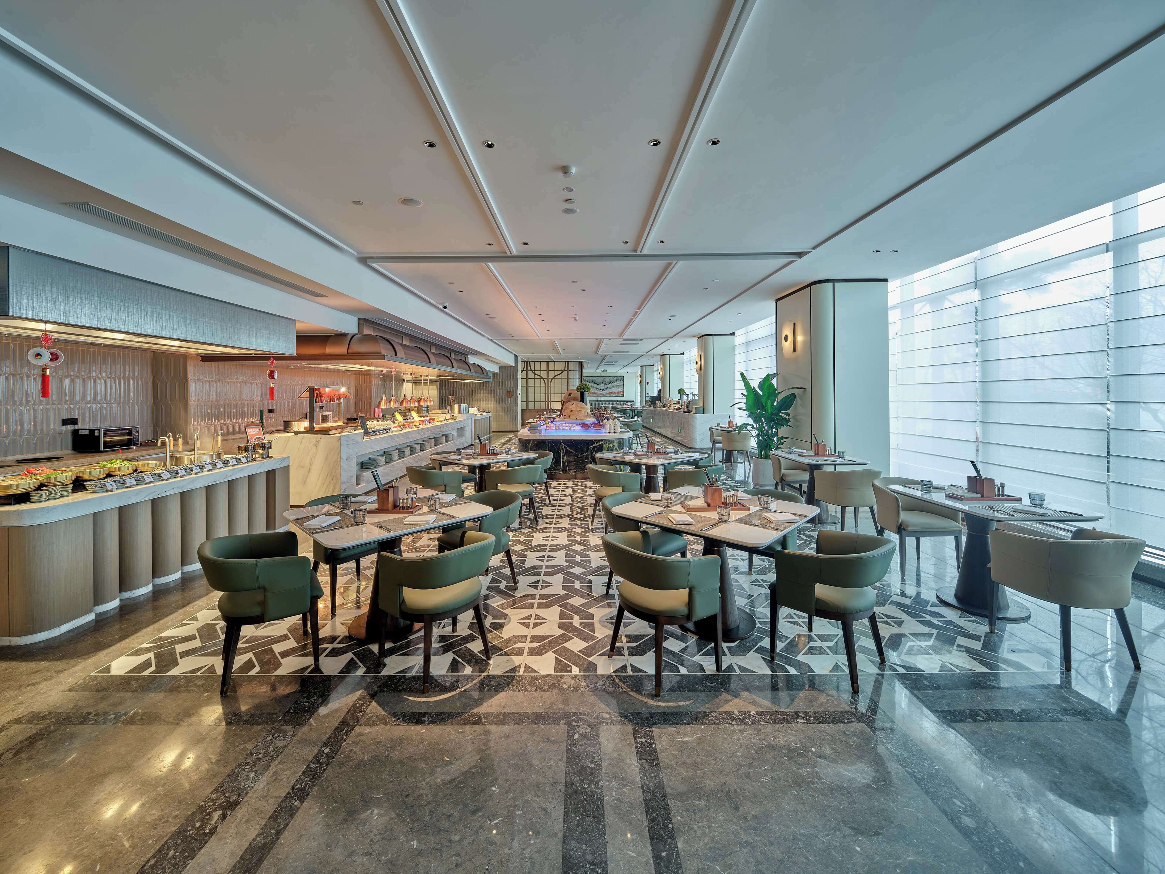 A spacious hotel lobby with a central bar area, multiple seating arrangements, and large windows providing natural light.