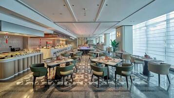 A spacious hotel lobby with a central bar area, multiple seating arrangements, and large windows providing natural light.
