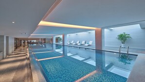 A modern indoor swimming pool with clear glass walls, a tiled floor, and a seating area with lounge chairs. - Doubletree By Hilton Yanji (Yanbian)