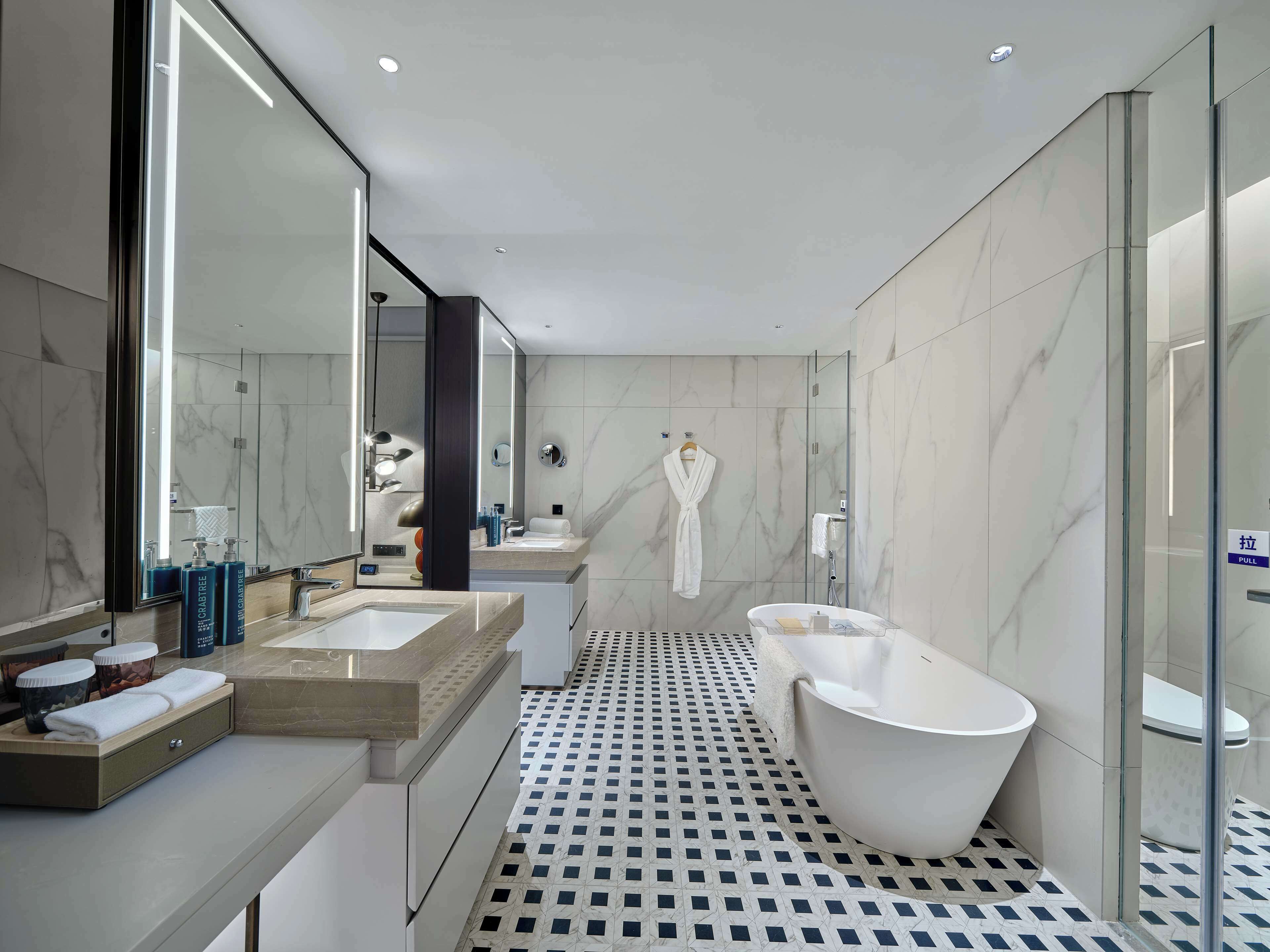 Een moderne badkamer met een vrijstaand bad, een grote spiegel en een wastafel met een marmeren aanrecht.
