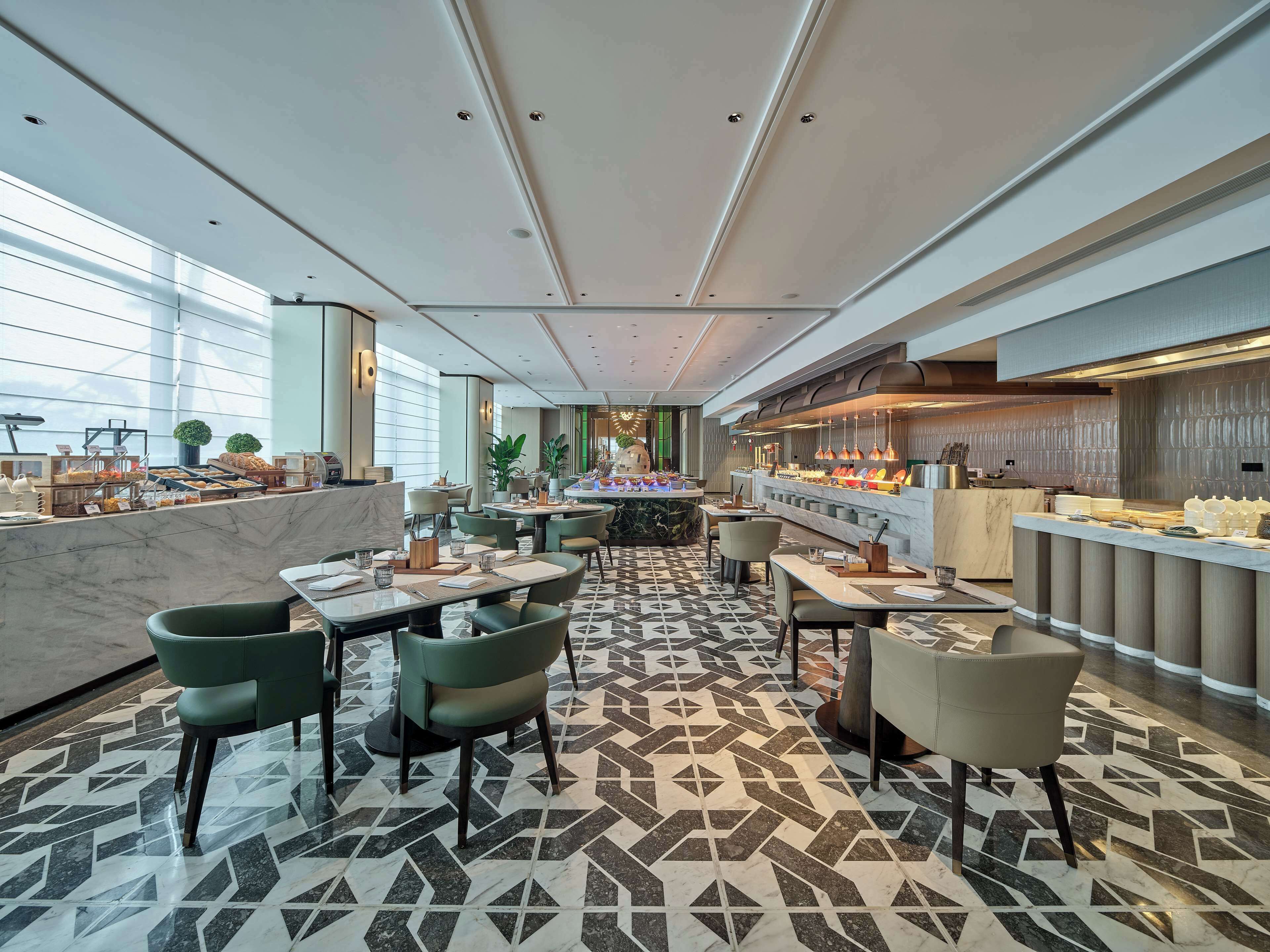 A modern restaurant with a marble counter, green chairs, and a patterned floor.