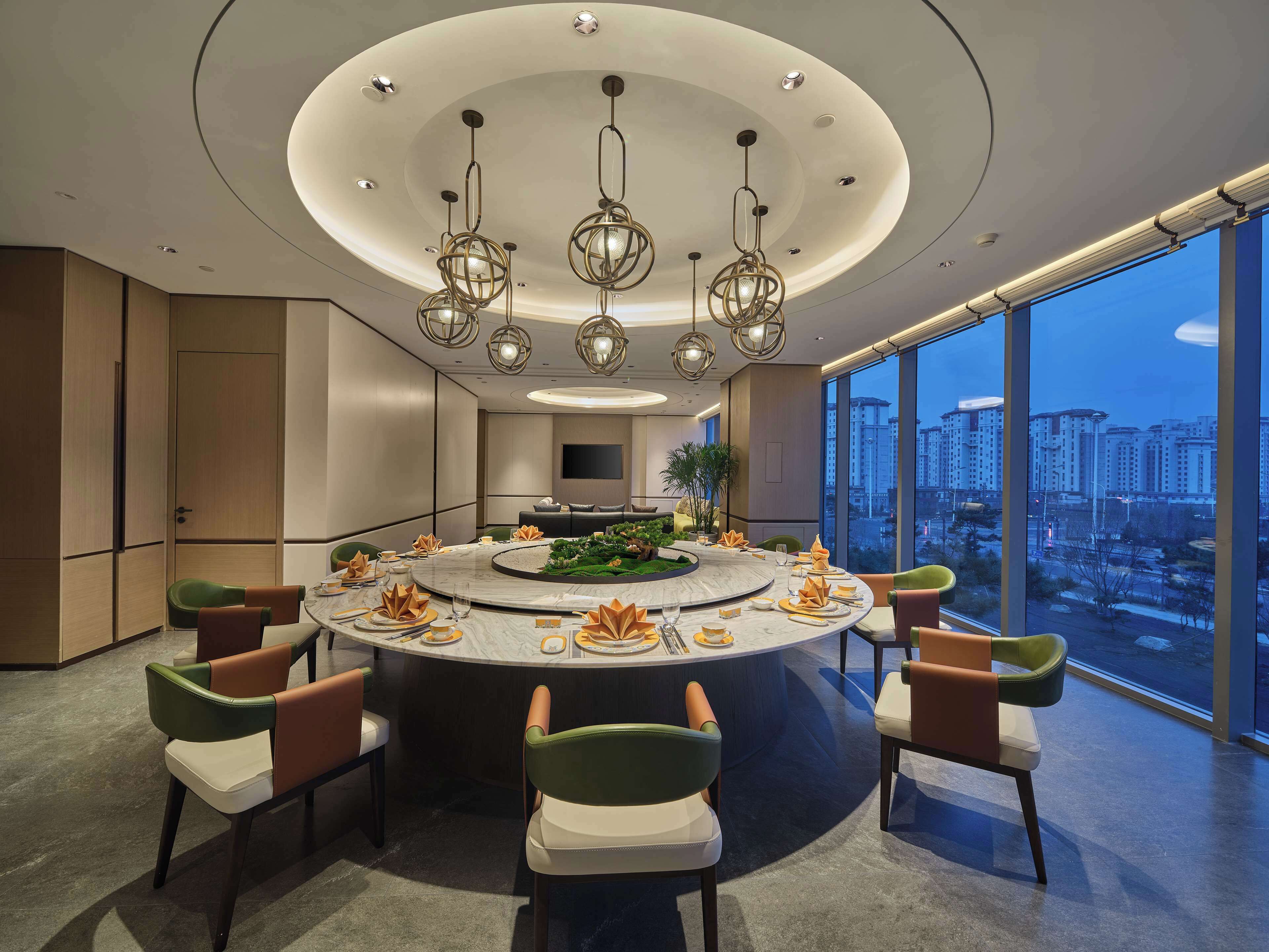 A modern dining area with a round table, chairs, and a city view through large windows.
