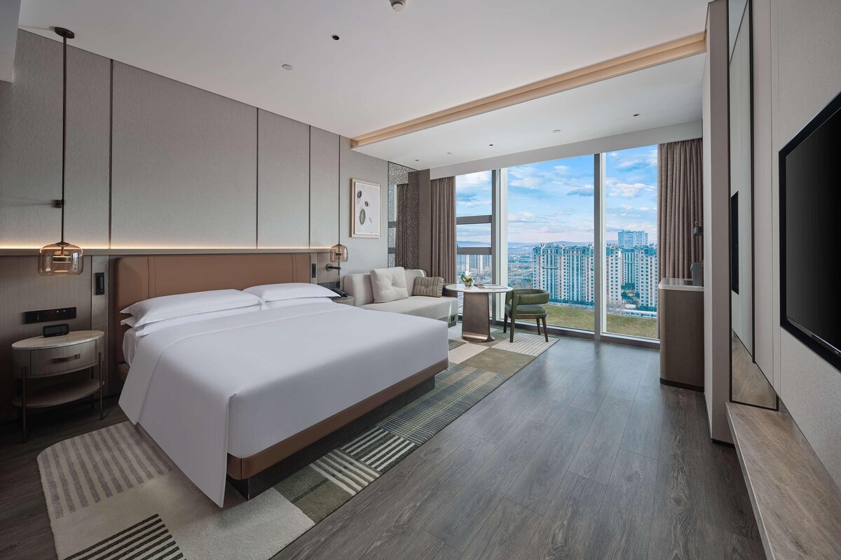 Una habitación de hotel moderna con una cama grande, un escritorio, una silla y un televisor.