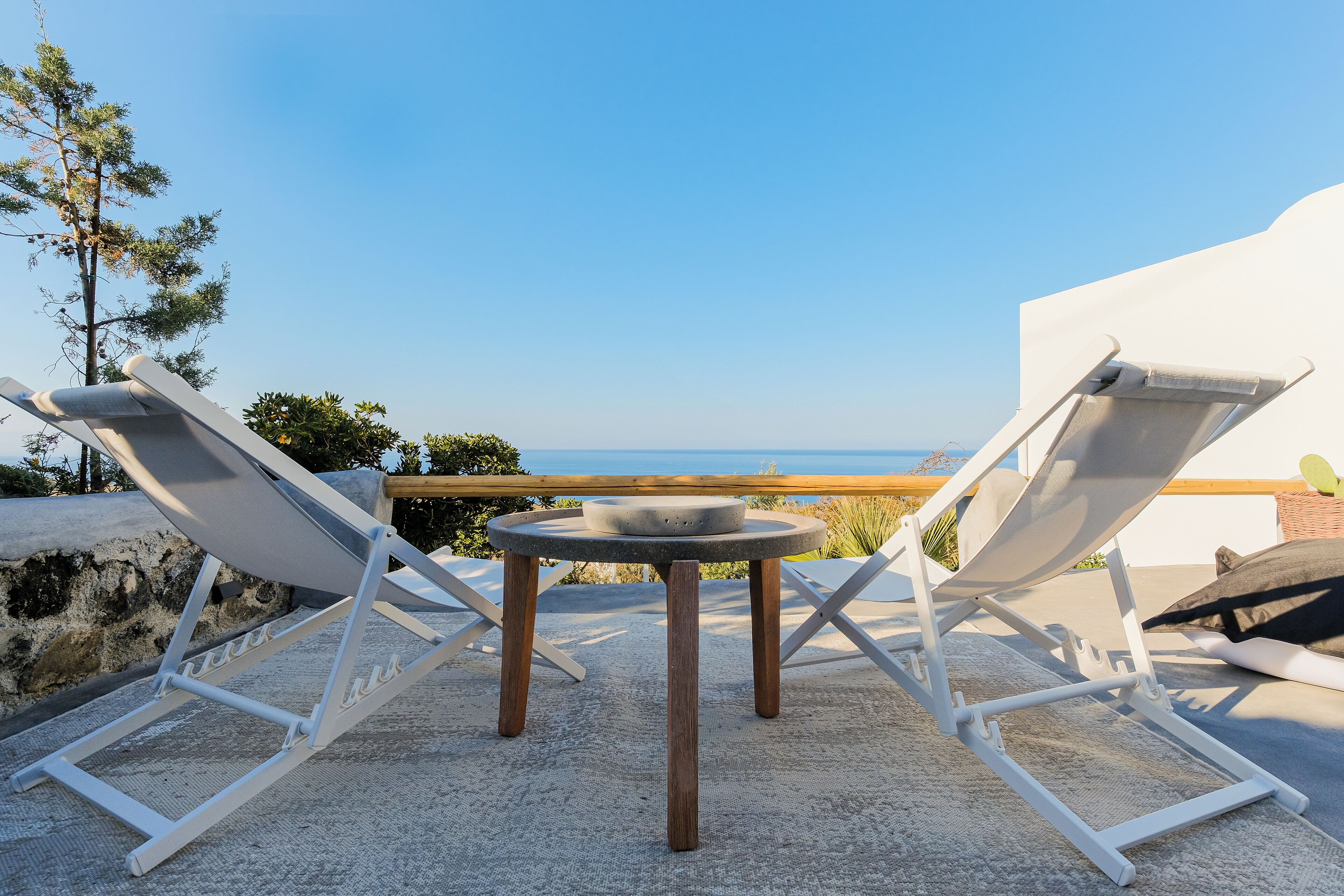 A terrace with two lounge chairs and a small table, overlooking a scenic view.