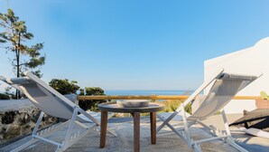 A terrace with two lounge chairs and a small table, overlooking a scenic view. - SunSea Living Suites (Santorini)