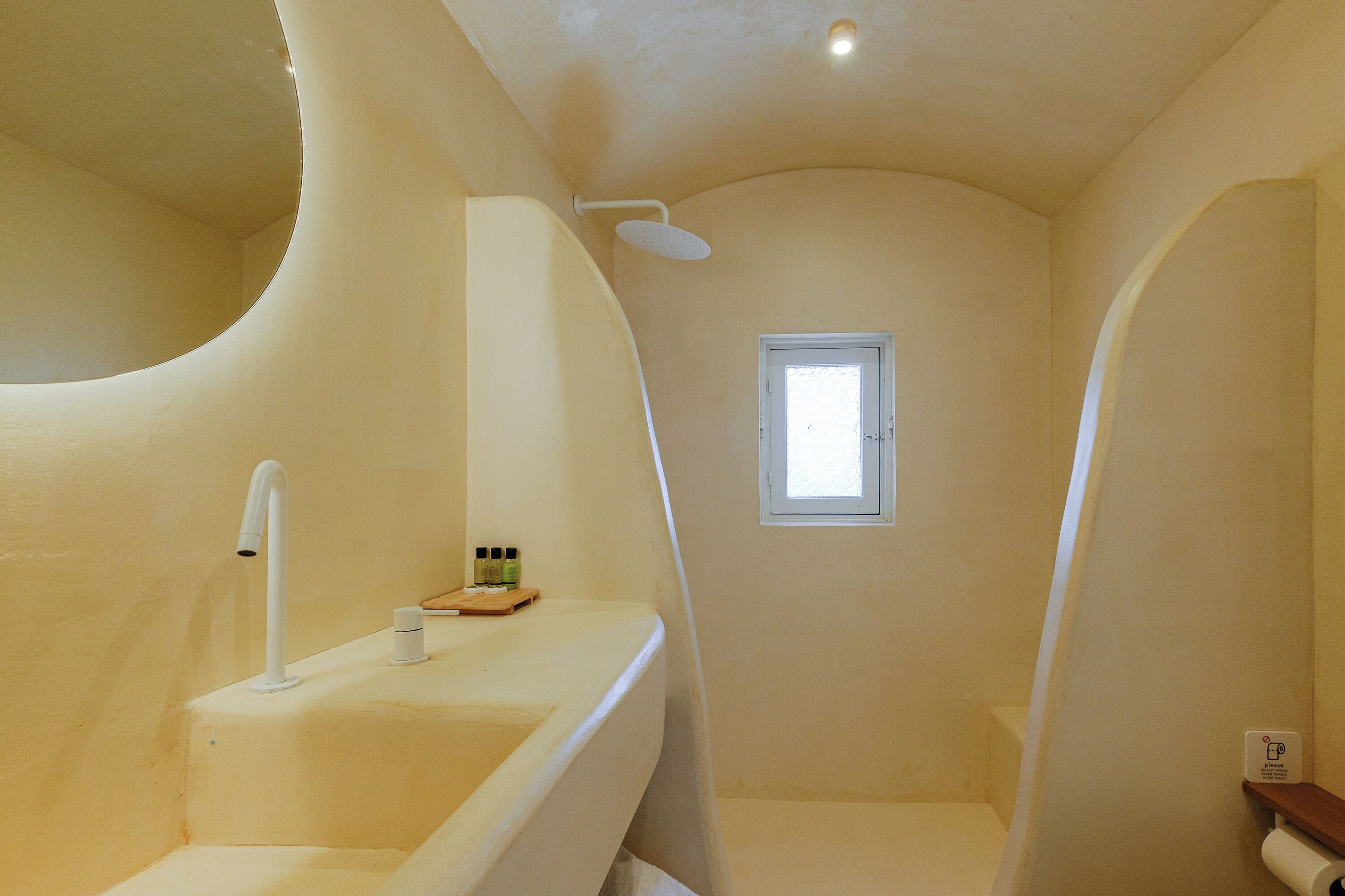 A bathroom with a curved wall, a shower, a sink, and a small window.