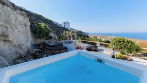 A swimming pool with a view of the sea and a white building in the background. - SunSea Living Suites (Santorini)