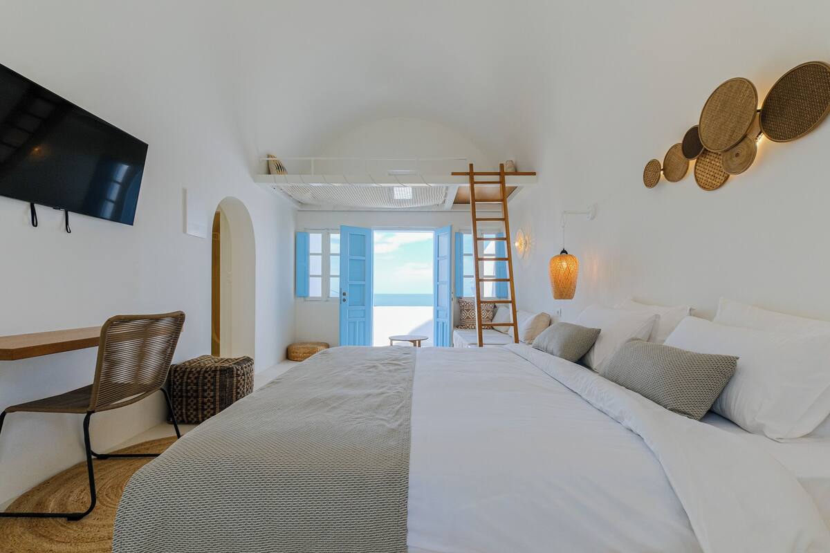 A bedroom with a bed, a chair, a TV, a ladder, and a view of the outside.