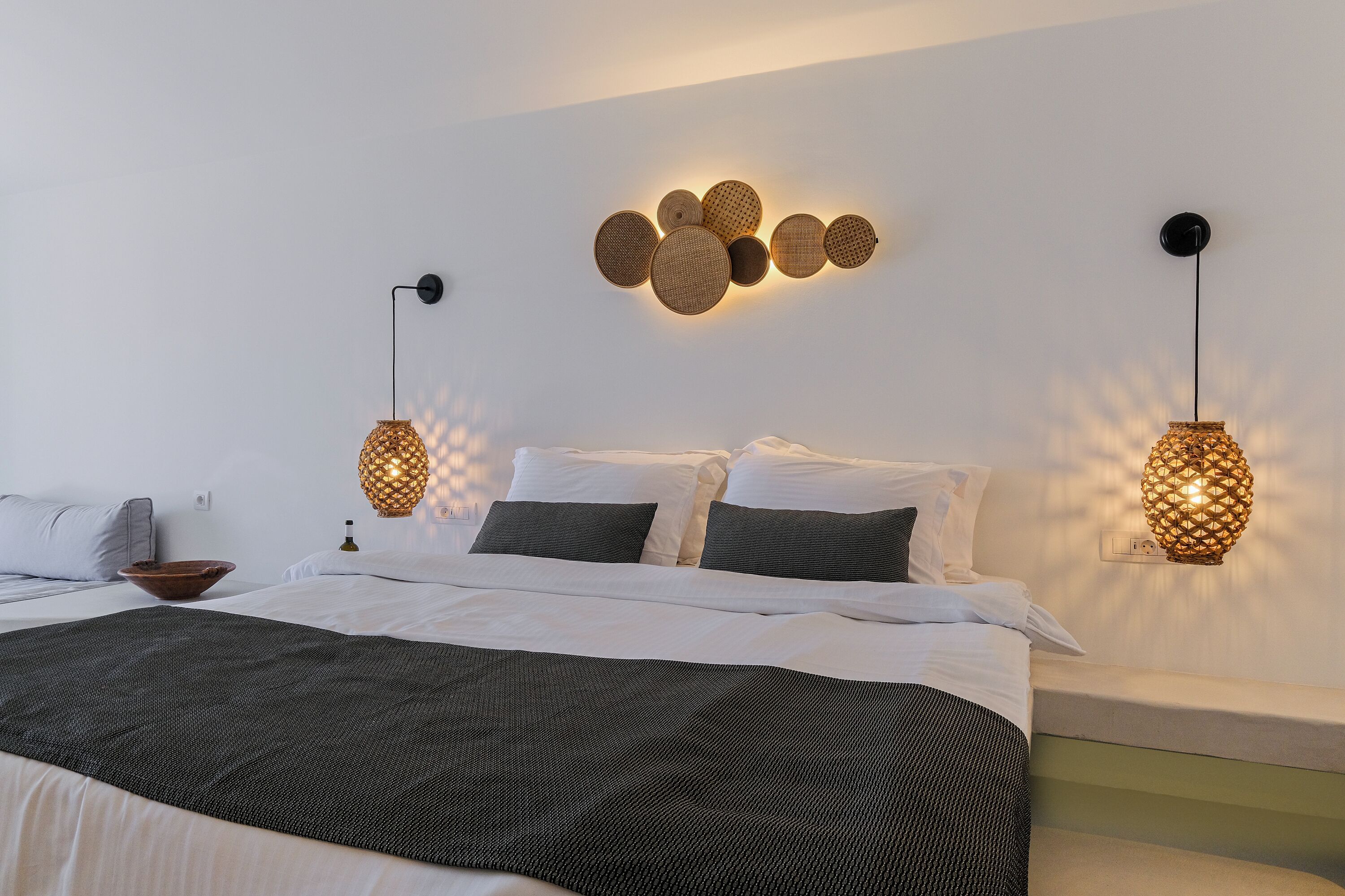 A modern hotel room with a neatly made bed, a wall-mounted light fixture, and a decorative wall piece.