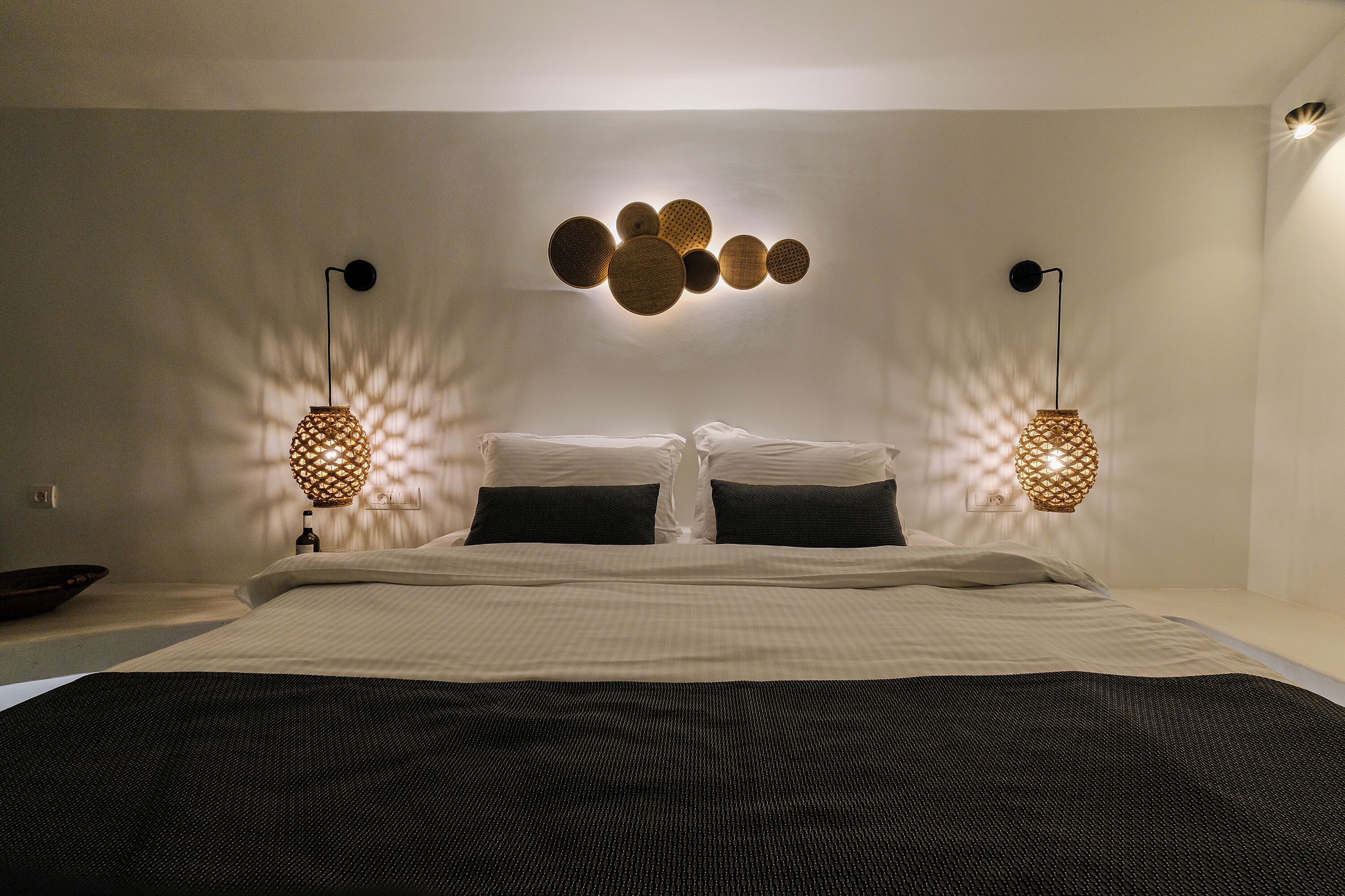 Een net opgemaakt bed met een geruit sprei, twee zwarte kussens en twee wandlampen met een geweven patroon.
