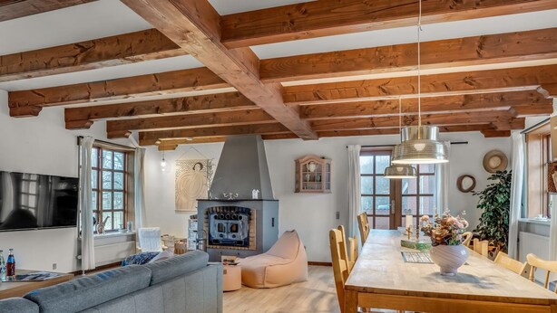 Un salon moderne avec un plafond en bois, une cheminée intégrée, un grand canapé, une table à manger avec des chaises et un téléviseur.