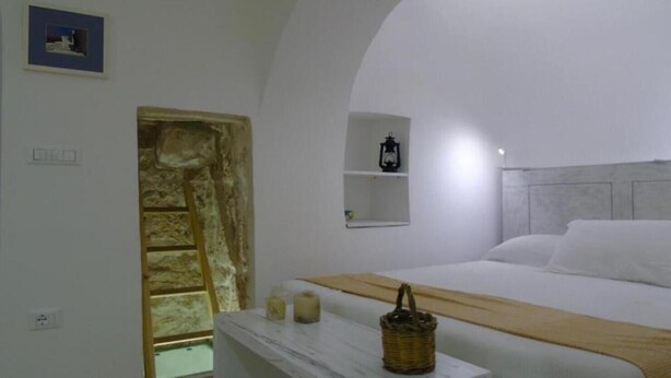 A bedroom with a bed, a nightstand, a wall-mounted shelf, and a stone wall.