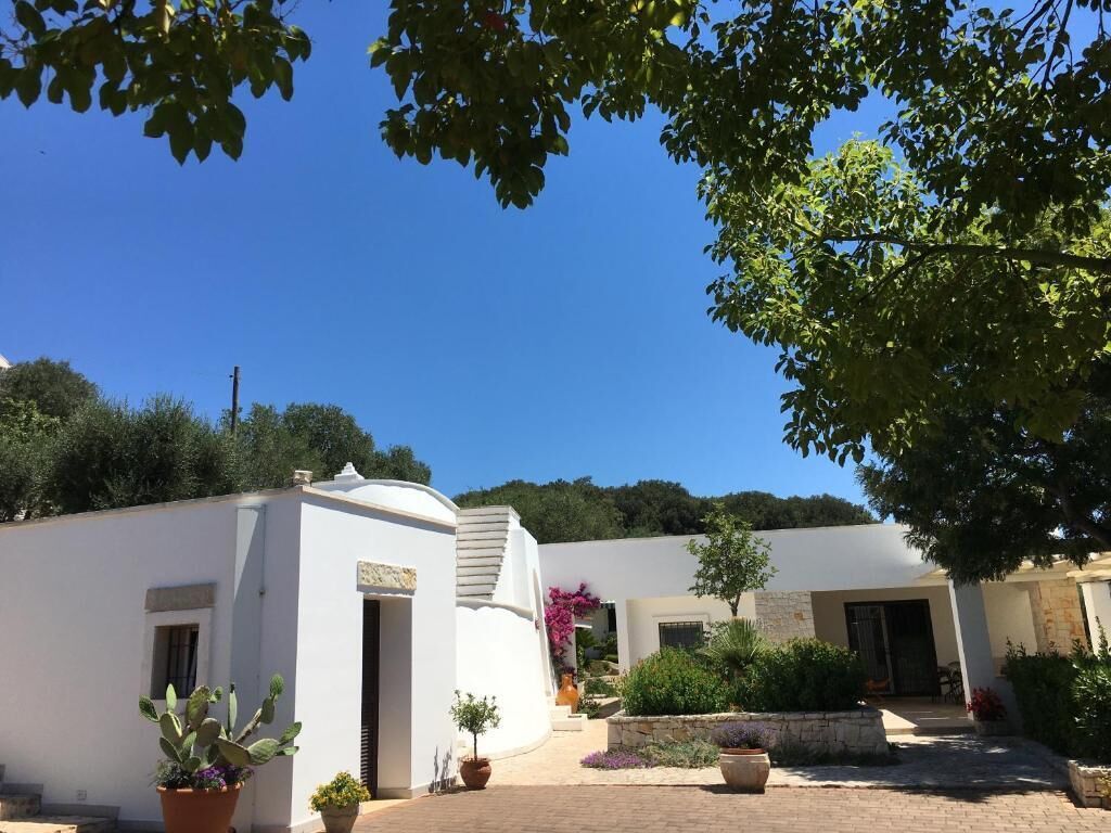 A white building with a curved facade, a paved courtyard, and potted plants.