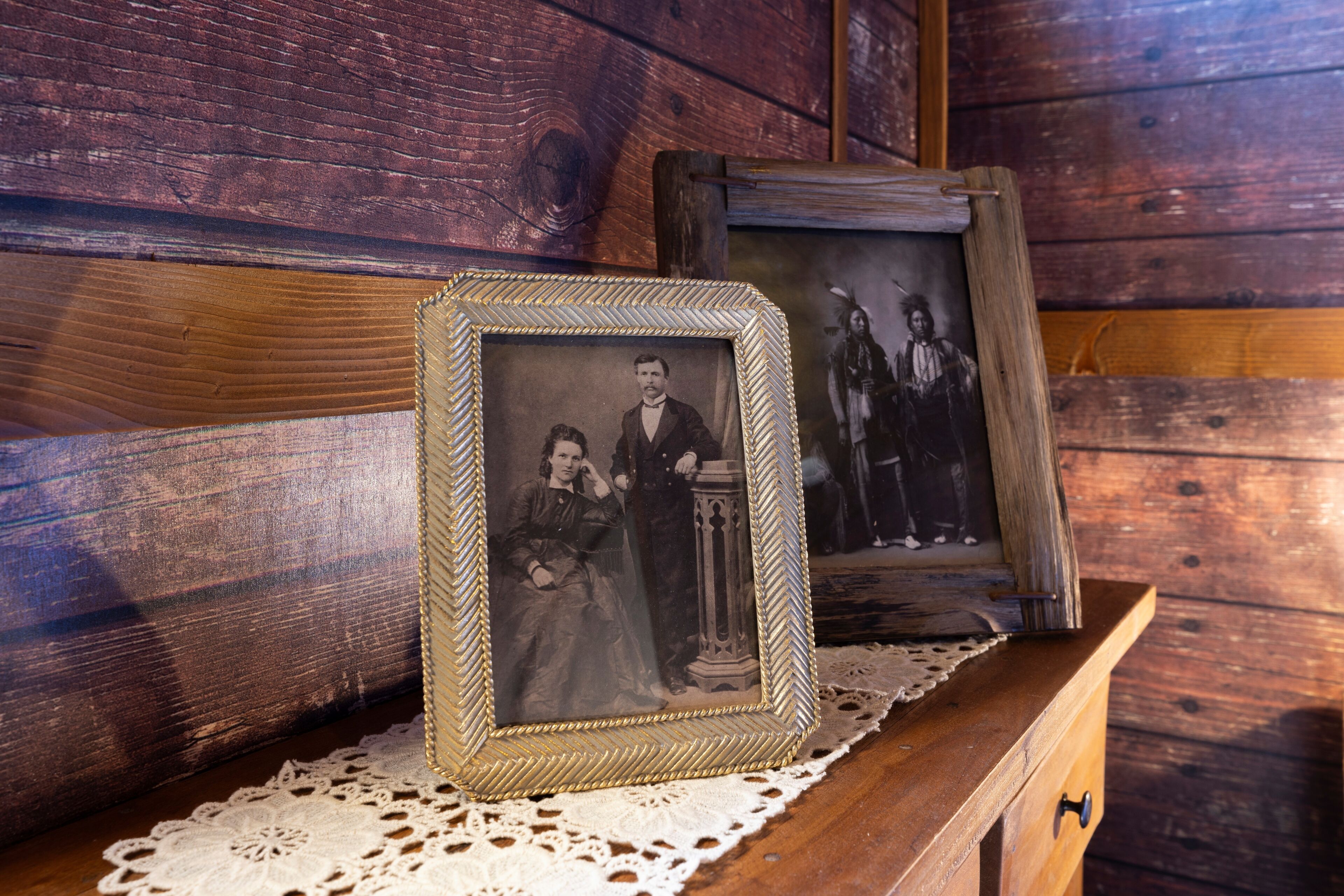 Une commode en bois ornée d’un chemin de table en dentelle et de deux photographies encadrées.