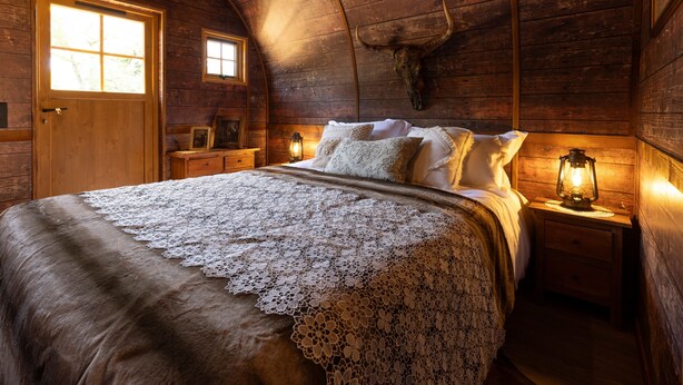 A cozy wooden room with a bed, a wooden door, a window, and a wall-mounted cow skull. - O'tel Park (Le Bernard)