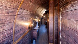 A narrow wooden corridor with a curved ceiling, a small table with a vase, and a metal bucket on the floor. - O'tel Park (Le Bernard)
