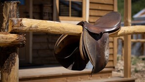 A wooden fence with a leather saddle hanging on it. - O'tel Park (Le Bernard)
