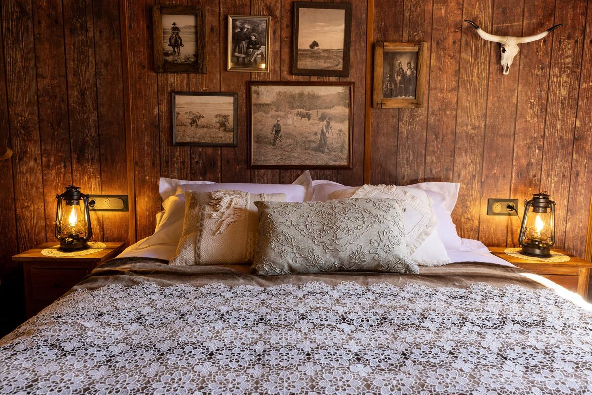 A wooden-paneled room with a bed, framed pictures, and a mounted cow skull.