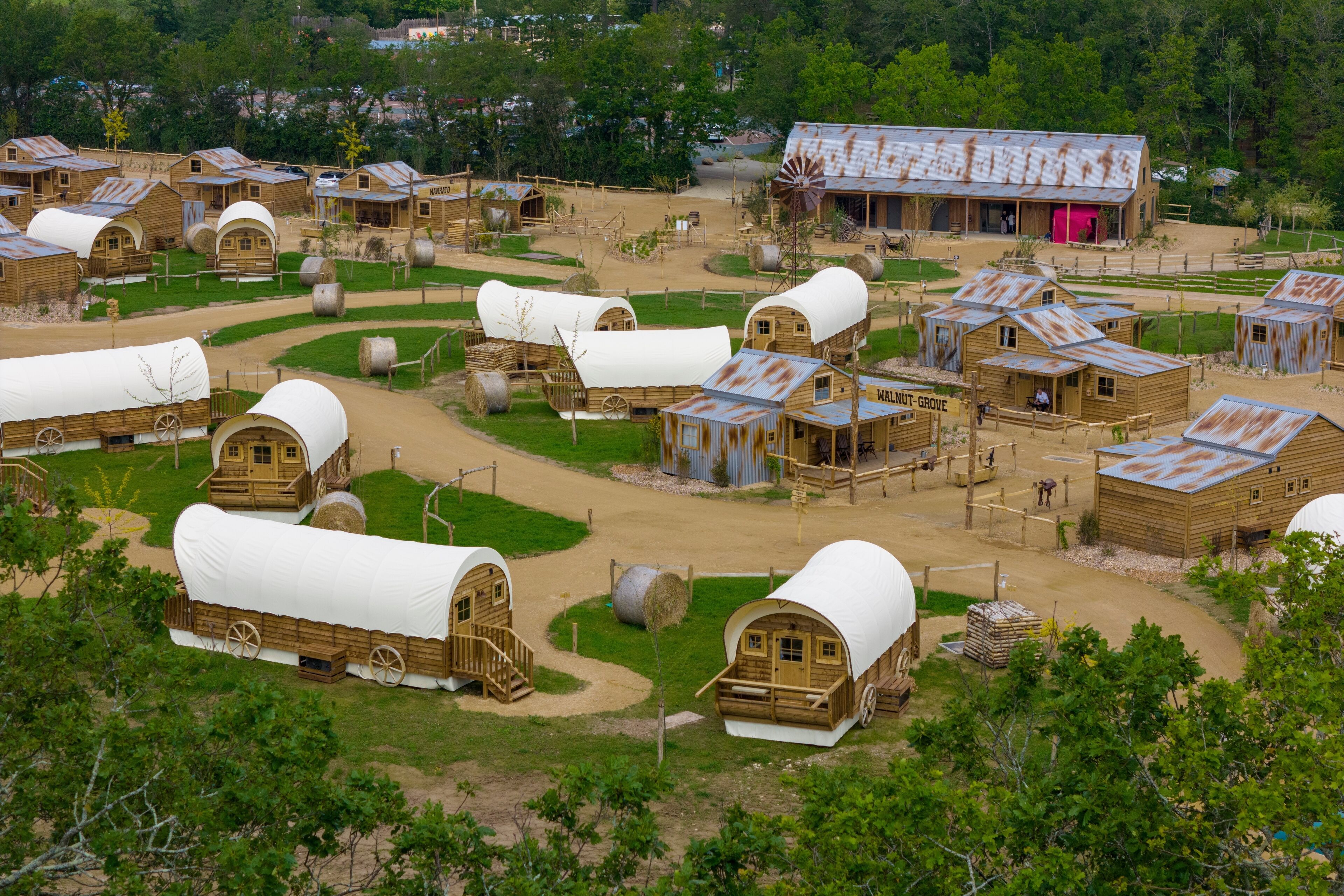 A rustic wooden building with a large windmill, surrounded by covered wagons and other wooden structures.
