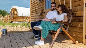 A wooden cabin with a porch, a covered wagon, and a wooden deck. - O'tel Park (Le Bernard)