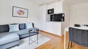 A modern living room with a grey sofa, a small round table, and a dining area with a black wicker chair.