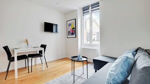 A modern living room with a white table, black chairs, a grey sofa, and a small round table with a candle.